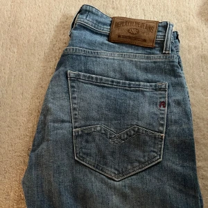 Blå jeans från Replay - Snygga blå jeans från Replay med klassisk femficksdesign och en diskret logga på bakfickan. De har en normal passform och är perfekta för en avslappnad stil. Märkeslappen i läder på baksidan ger en extra touch av stil.