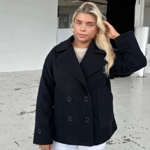 Svart kappa  - Snygg svart kappa med dubbelknäppning och breda slag. Jackan har en klassisk design med stora knappar och långa ärmar. Perfekt för en stilren look.