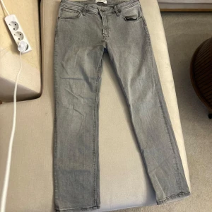 Grå jeansbyxor - Snygga grå jeansbyxor med en klassisk femficksdesign. De har en rak passform och är perfekta för en avslappnad stil. Byxorna har en knapp och dragkedja framtill.