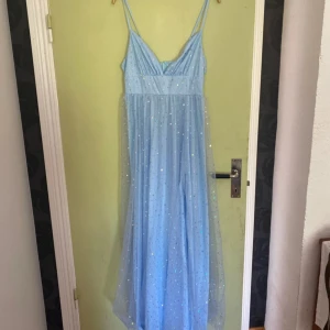 Ljusblå glittrig långklänning - Säljer en magisk ljusblå långklänning med tunna axelband och glittrande detaljer. Perfekt för en speciell kväll med sitt skimrande tyg och eleganta fall. Klänningen har en v-ringad design och ger en drömlik känsla. Passar perfekt för att glänsa på festen! ✨ Den är bara testad 