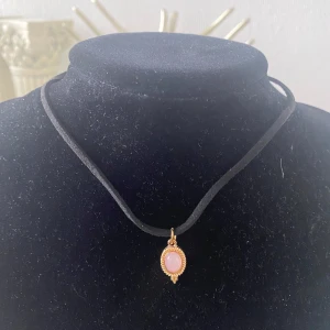 Hänge Halsband Kedje  - Elegant halsband med ett svart band och ett vackert rosa hänge i guldinfattning. Hänget har en oval form och ger en stilren look. Perfekt för att lägga till en touch av färg och elegans till din outfit.  Helt ny,  70kr/st 