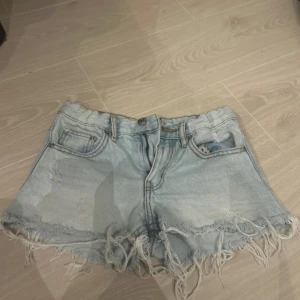 Lågmidjade jeans shorts  - Säljer ett par ljusa jeansshorts med fransiga kanter och slitna detaljer. De har en klassisk femficksdesign och knappgylf. Perfekta för en avslappnad stil. I strl 134 men passade mig förra året