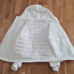 Vit quiltad cardigan med huva - Säljer en stilren vit jacka med huva och dragkedja. Jackan har ett quiltat mönster och långa ärmar. Perfekt för kyligare dagar. Den har praktiska fickor med dragkedjor för säker förvaring.