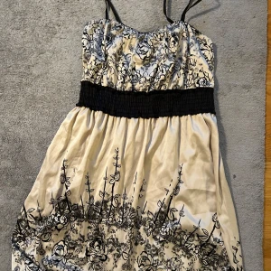 Blommig klänning från Vila - Säljer en söt klänning från Vila med svart blommönster på en vit bakgrund. Klänningen har smala axelband och en elastisk midja för en bekväm passform även en ballong form nedtill. Perfekt för sommarens alla tillfällen!💯