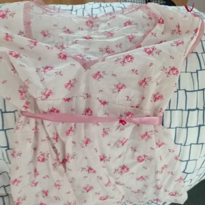 Blommig pyjamas från Passionata - Sött blommigt pyjamasset från Passionata i ljusrosa med små röda blommor. Toppen har en v-ringad hals och ett rosa band i midjan för en feminin touch. Perfekt för somriga dagar! Köpt begagnad för 170kr men använd bara en gång 