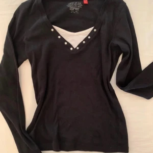 Svart söt topp - Snygg svart långärmad tröja från Esprit med v-ringning och dekorativa knappar. Perfekt för en stilren look. Tröjan har en vit detalj vid halsen som ger en lager-på-lager-effekt.