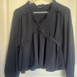 Mörkblå blus från Missay  - Säljer en elegant mörkblå blus från Missay med volangdetaljer och v-ringning. Blusen har långa ärmar och en lös passform, perfekt för en stilren look. Passar bra till både jeans och kjol.