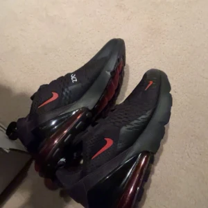 Nike Air Max 270 i svart och röd - Snygga Nike Air Max 270 sneakers i svart med röda detaljer. Skorna har en synlig Air-enhet i hälen för extra komfort och stil. Perfekta för både träning och vardag. Skorna är helt oanvända, säljer för köpte fel storlek och glömde skicka tillbaka. Skorna är också 100% äkta 