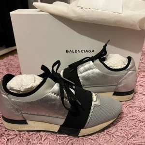 Balenciaga sneakers - Silvriga Balenciaga sneakers med svarta detaljer i modellen race runner. Skorna är använda flitigt därav priset. Själva skon är i relativt gott skick men sulan har lite fläckar som syns på bilderna. Köpta på balenciaga butiken i köpenhamn. Box, dustbag och kvitto medföljer!