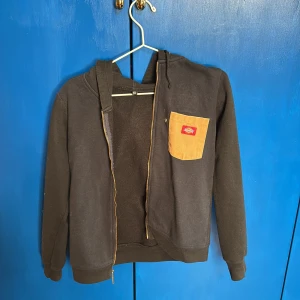 Svart hoodie från Dickies - Säljer en svart hoodie från Dickies med dragkedja och en kontrasterande beige ficka på bröstet. Hoodien har långa ärmar och en praktisk huva. Mycket skön och passar till det mesta ❤️