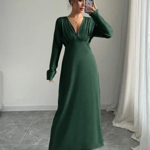 Grön långklänning med v-ringning - Elegant grön långklänning med djup v-ringning och långa ärmar. Klänningen har en smickrande passform och är perfekt för speciella tillfällen. Den är tillverkad i ett mjukt och följsamt material som ger en lyxig känsla.