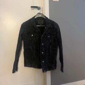 Svart jeansjacka med silvriga knappar lager 157 - Snygg svart jeansjacka med klassisk krage och silvriga knappar framtill. Jackan har två bröstfickor med lock och knapp, samt raka sömmar.