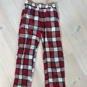 Röd-rutiga pyjamasbyxor från Lindex - Supermysiga pyjamasbyxor från Lindex i röd, vit och grön rutig design. Byxorna har resår och snörning i midjan för skön passform. Perfekta för chill hemma eller som pyjamasbyxor. Tillverkade i mjukt bomullstyg.