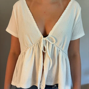 Vit omlottopp med knyt och v-ringning - Superfin vit omlottopp med djup v-ringning fram från lager 157. Kortärmad och lätt utsvängd nertill, perfekt till jeans eller kjol. Enkel men ändå unik detalj  med knyt. Man kan ha toppen på båda håll. Säljer pga av att den inte kommer till användning! Priset kan diskuteras!❤️