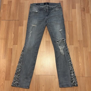 Grå bootcut jeans med zebradetalj LTB - Grå jeans från LTB i bootcut-modell med coola zebramönstrade paneler längs bensluten. Jeansen har slitna detaljer och trasiga partier framtill för en edgy vibe. Tillverkade i klassiskt denimtyg och perfekta för dig som vill sticka ut. dessa är själv utsydda men passar tyvärr ej, är aldrig använda! de är väldigt fina och edgy. pris kan diskuteras o skriv vid frågor💓☺️