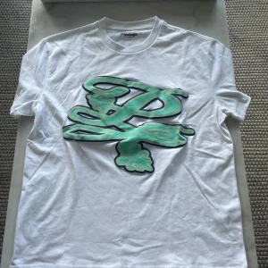 Vit t-shirt från Prèstanza med tryck - Vit t-shirt från Prèstanza med stort mintgrönt och svart tryck framtill och mindre logga bak. Klassisk rund hals och korta ärmar. Skön och lätt i bomull, perfekt till jeans eller shorts.