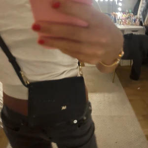 Svart axelväska Michael Kors - Snygg svart axelväska från Michael Kors med guldfärgade detaljer och MK-logga framtill. Väskan är i stilren design med justerbar axelrem och tillverkad i skinn. Perfekt storlek för det viktigaste och passar till många outfits.