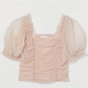 Puffärmad rosa blus i mesh - Supersöt ljusrosa blus med puffärmar och transparent mesh. Toppen har rynkade detaljer framtill och små prickar i tyget som ger en extra touch. Fyrkantig urringning och kort, croppad passform. 