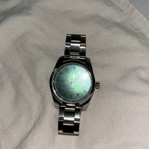 Silver klocka med gröna detaljer - Säljer min klocka som jag fick i present. Den är alldeles för stor på mig och jag vill bli av med den. Vet inte vilket märke eller storlek men den är gjord i stainless steel. Osäker på priset av den men mitt pris är inte hugget i sten. Man kan fixa storleken då den har totalt 6st avtag bara delar, men jag har inte pengarna för att göra det.
