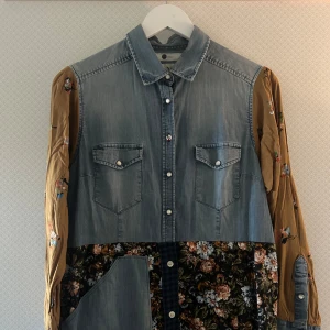 Patchwork klänning från Boomerang - Unik långklänning från Boomerang x Studio Fogelberg med jeansliv, bruna blommiga ärmar och kjol i blommigt och rutigt tyg. Knäppning framtill, två bröstfickor och cool mix av denim och mönster.