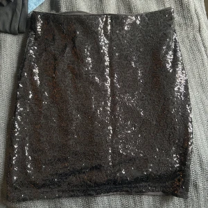 Svart paljettkjol i kort modell - Supersnygg svart kortkjol täckt med glittrande paljetter. Kjolen har en rak passform och kan användas som topp oxå (se bild 2). Knappt använd!