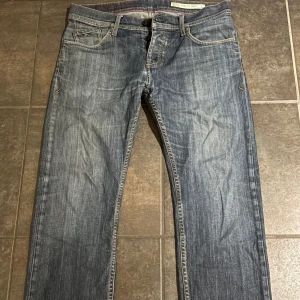 Tommy hilfigier jeans - Snygga blå jeans från Hilfiger Denim med klassisk femficksdesign och diskreta slitningar. Jeansen har raka ben och normal passform, med tydliga kontrastsömmar och Hilfiger-detaljer på bakfickan. Perfekta för en avslappnad stil.