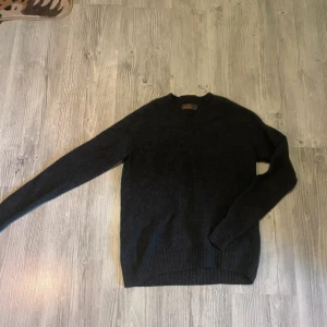 Mörkgrå ulltröja från Morris - Snygg mörkgrå stickad tröja från Morris i klassisk modell med v-ringning. Tillverkad i mjuk ull som håller dig varm under kyliga dagar. Perfekt för dig som gillar stilrena och tidlösa plagg. Långärmad och med ribbade muddar för extra komfort.