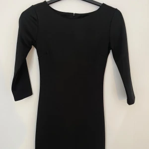 Svart enkel klänning med trekvartsärm - Stilren svart klänning med trekvartsärm och rund halsringning. Figurnära passform och klassisk design som passar perfekt till många tillfällen. Dragkedja bak för enkel påklädning.