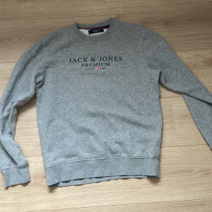 Grå sweatshirt från Jack & Jones - Säljer en stilren grå sweatshirt från Jack & Jones Premium med tryckt logga på bröstet. Tröjan har rund halsringning, långa ärmar och ribbade muddar. Perfekt för en chill och avslappnad look. Kom privat för att diskutera vidare priset 😊
