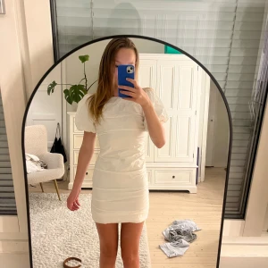 Vit kort puffärmad klänning - Supersöt vit kort klänning med puffärmar och öppen rygg. Tight passform med lätt rynkade detaljer längs sidorna. Perfekt för dig som vill ha en stilren och trendig look med en twist. Materialet känns lätt och passar bra till varmare dagar. Klänningen är i storlek 32, dock har den sytts in i midjan så den passar toppen för dig som är ca 158-165 cm lång. Jag har stlk xxs/xs och den passar mig perfekt. Inga defekter, använd 1 gång💕