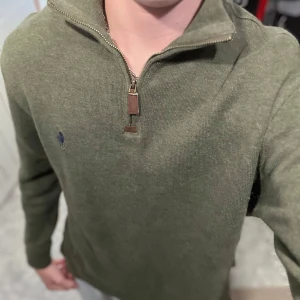 Olivgrön half zip tröja Polo Ralph Lauren - Snygg olivgrön långärmad tröja från Polo Ralph Lauren med half zip och klassisk broderad logga på bröstet. Tröjan är i mjuk bomull och har en stilren, normal passform. Perfekt till jeans eller chinos för en clean look.