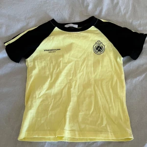 Gul och svart t-shirt från Bambi - Gul t-shirt med svarta raglanärmar från Bambi.  Perfekt för dig som gillar sportig och avslappnad stil.