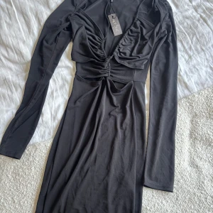 Svart långärmad klänning NLY ONE XS - Helt oanvänd svart långärmad klänning från NLY ONE i figurnära modell. Klänningen har snygga rynkade detaljer framtill, cut out vid midjan och djup v-ringning. Tillverkad i mjukt stretchigt material.