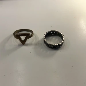 Två coola ringar i guld och silver - Säljer två unika ringar: en i guld med en öppen triangel-design och en i silver med detaljerat mönster runt hela ringen. Perfekta för att ge din stil en edgy touch!