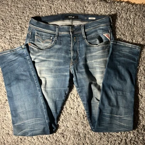 Replay Anbass jeans - Säljer ett par Replay Anbass jeans i klassisk blå tvätt med snygga slitningar och kontrastsömmar. Modellen har fem fickor, normal passform och raka ben. Perfekta för dig som gillar en avslappnad men stilren look. Replay Anbass jeans i storlek 33/32. Mycket bra skick förut att det finns hål vid det vänstra knäet. Kom privat för bild. Nypris runt 1800kr, mitt pris 250kr. Kontakta mig om du har frågor✅