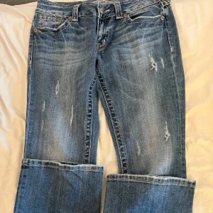 Miss Me blå bootcut jeans med detaljer - Snygga blå jeans från Miss Me med bootcut passform och slitna detaljer. Jeansen har dekorativa bakfickor med broderier, metallknappar och emblem. Klassisk femficksmodell i jeansmaterial med kontrastsömmar och coola detaljer på fickorna.💕 Inga slitningar