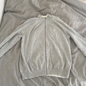 Grå kofta från Polo Ralph Lauren - Snygg grå kofta från Polo Ralph Lauren med hel dragkedja framtill och diskret logga på bröstet. Använd max 2 gånger, vill sälja för den är lite för stor för mig . (Pris kan diskuteras)