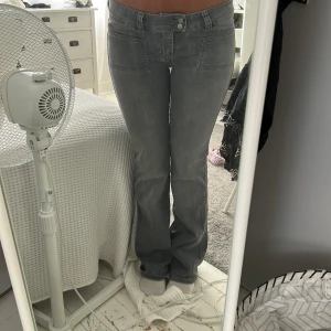 Grå bootcut jeans med fickor - Säljer ett par gråa jeans med bootcut-modell och stora framfickor. Jeansen har hög midja och raka ben med lätt utsvängning nertill. Snygg tvätt och klassisk look, perfekta till sneakers eller boots.