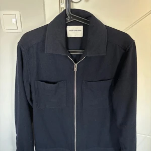 overshirt från These Glory Days - Stilren svart overshirt från These Glory Days med två stora bröstfickor och dragkedja framtill. Jackan har klassisk krage och är långärmad, perfekt för lager-på-lager. Materialet är mjukt och känns lyxigt, passar till många olika outfits.