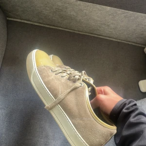 Beige sneakers från Lanvin  - Snygga beige mocka skorf i från Lanvin i storlek 43/44 med unika lackade tår i ljusgul ton. Skorna har snörning, rund tå och vit platt sula. Perfekta för dig som vill sticka ut med en lyxig och stilren look. (OBS snörrena är trasiga) I skon står de strolek uk 9