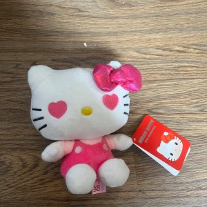 Hello kitty - Det här är en Hello Kitty-mjukisdocka med hjärtformade ögon och en rosa klänning. Perfekt för samlare eller som en söt present till någon som älskar kawaii-stil. Dockan har en glittrig rosa rosett och är liten nog att ta med överallt.