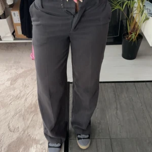 Svarta vida kostymbyxor weekday - Säljer ett par svarta kostymbyxor med vid passform och klassisk look. Byxorna har hög midja och raka ben, perfekta för en clean och stilren outfit. Materialet känns mjukt och följsamt, och de har dragkedja framtill.