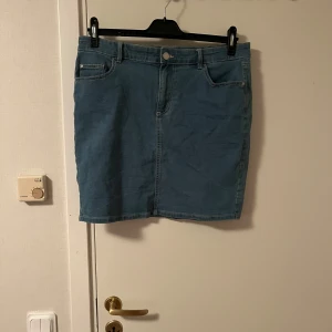 Blå jeanskjol Jane Skirt XL - Snygg blå jeanskjol från Jane Skirt i klassisk femficksmodell. Kjolen har normal passform, bälteshällor och dragkedja framtill. Perfekt till sneakers eller boots för en chill look.