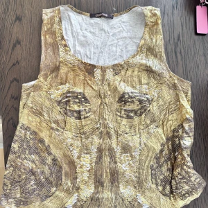 Guldig linnetopp från Roberto Cavalli - Unik linnetopp från Roberto Cavalli med ett iögonfallande guldmönster som ger en lyxig känsla. Toppen är ärmlös och har rund halsringning. Materialet är mjuk bomull och trycket har en skimrande effekt som sticker ut.