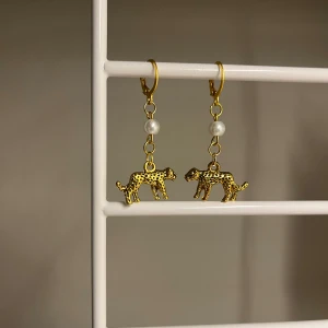 Guldiga leopardörhängen med pärldetalj - Unika örhängen i guld med leopardhänge och en söt vit pärla ovanför. Djurmönstret ger en cool vibe och detaljerna gör dem till ett statement. Perfekta för dig som vill sticka ut och addera lite edge till din stil. Handgjort 