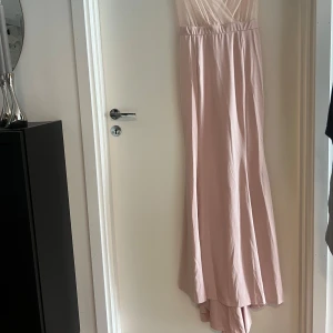 Ljusrosa långklänning med v-ringning - Elegant ljusrosa långklänning med djup v-ringning och tunna axelband. Överdelen är i ett skirt, glittrigt tyg. Kjolen är slät och faller snyggt längs kroppen. Funkar för S och M