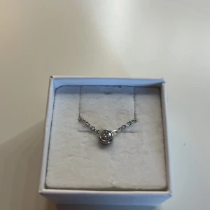 Silverhalsband med rund sten - Ett stilrent halsband i silverfärg med en tunn kedja och ett runt hänge med en glittrande sten i mitten. Perfekt för dig som gillar minimalistiska smycken med en touch av elegans.