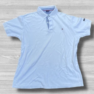 Tommy Hilfiger XXL piké - Snygg pikétröja från Tommy Hilfiger med klassisk krage, knappar och diskret logga på bröstet. Ärmarna är korta och materialet är mjuk bomull. Insidan av kragen har blåvitrandigt tyg för extra detalj. Perfekt för en clean och fräsch stil.