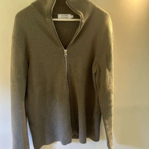 Olivgrön ribbad kofta från Ljung - Säljer en olivgrön ribbad kofta från Ljung med hel dragkedja framtill och hög krage. Tröjan är stickad i mjukt material och har långa ärmar. Perfekt för lager-på-lager och chill stil.