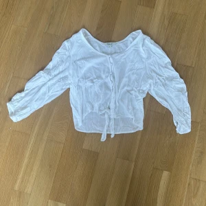 Vit blus med knyt från Kappahl - Supersöt vit blus från Kappahl i storlek S. Modellen är croppad med långa ärmar, knyt framtill och klädda knappar. Tunt och lätt material, perfekt för en chill look. 